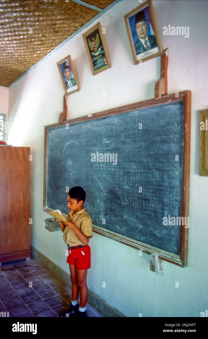 Indonesia, Jakarta. Boy reading aloud in front of portraits of the first and second president of Indonesia, Sukarno and Suharto. Stock Photo