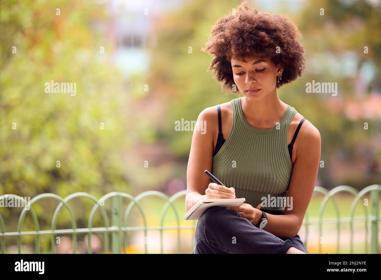 Young Woman Outdoors In Park Sitting On Bench Working Writing In Notebook Stock Photo