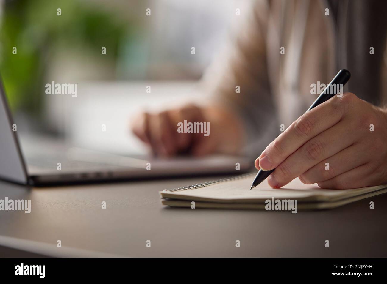 Close Up Of Man At Desk With Laptop Making Notes In Notebook Stock Photo