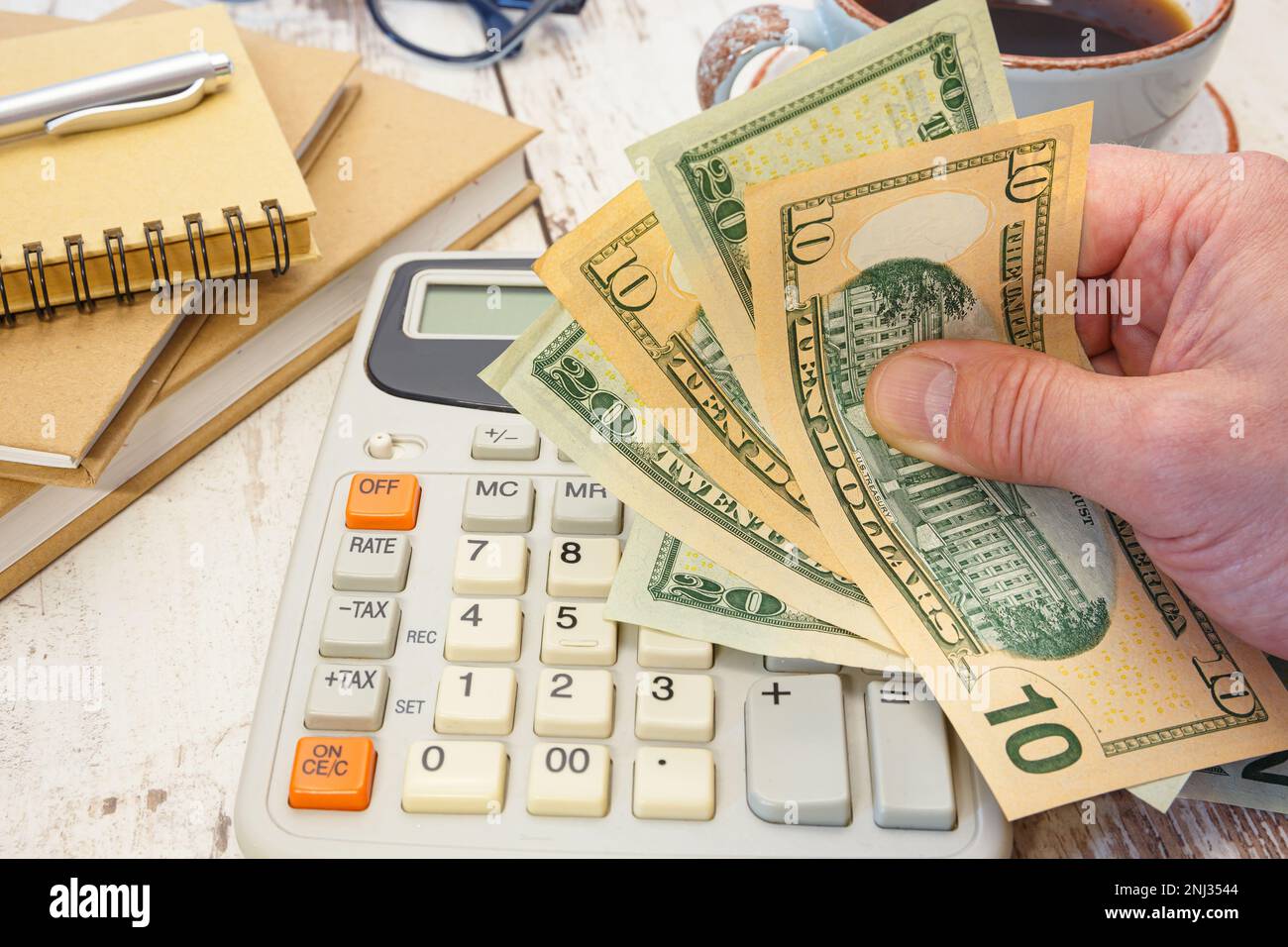Money in hand next to a calculator and office supplies. Financial
