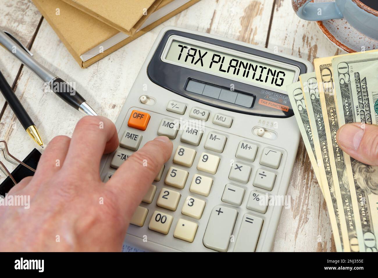 Money in hand next to a calculator and office supplies. TAX PLANNING