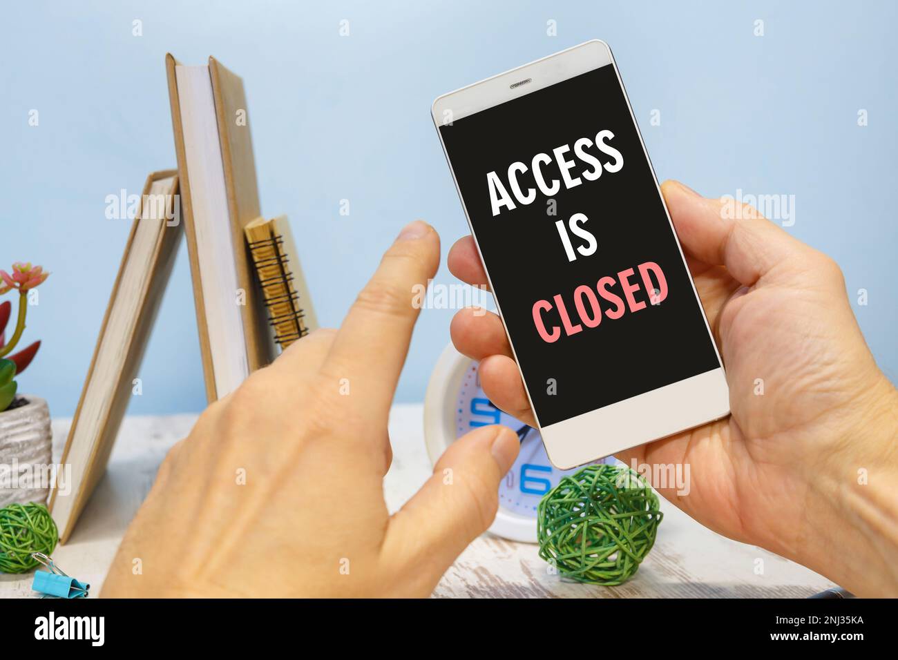 Smartphone in hand with the inscription ACCESS IS CLOSED next to office supplies Stock Photo