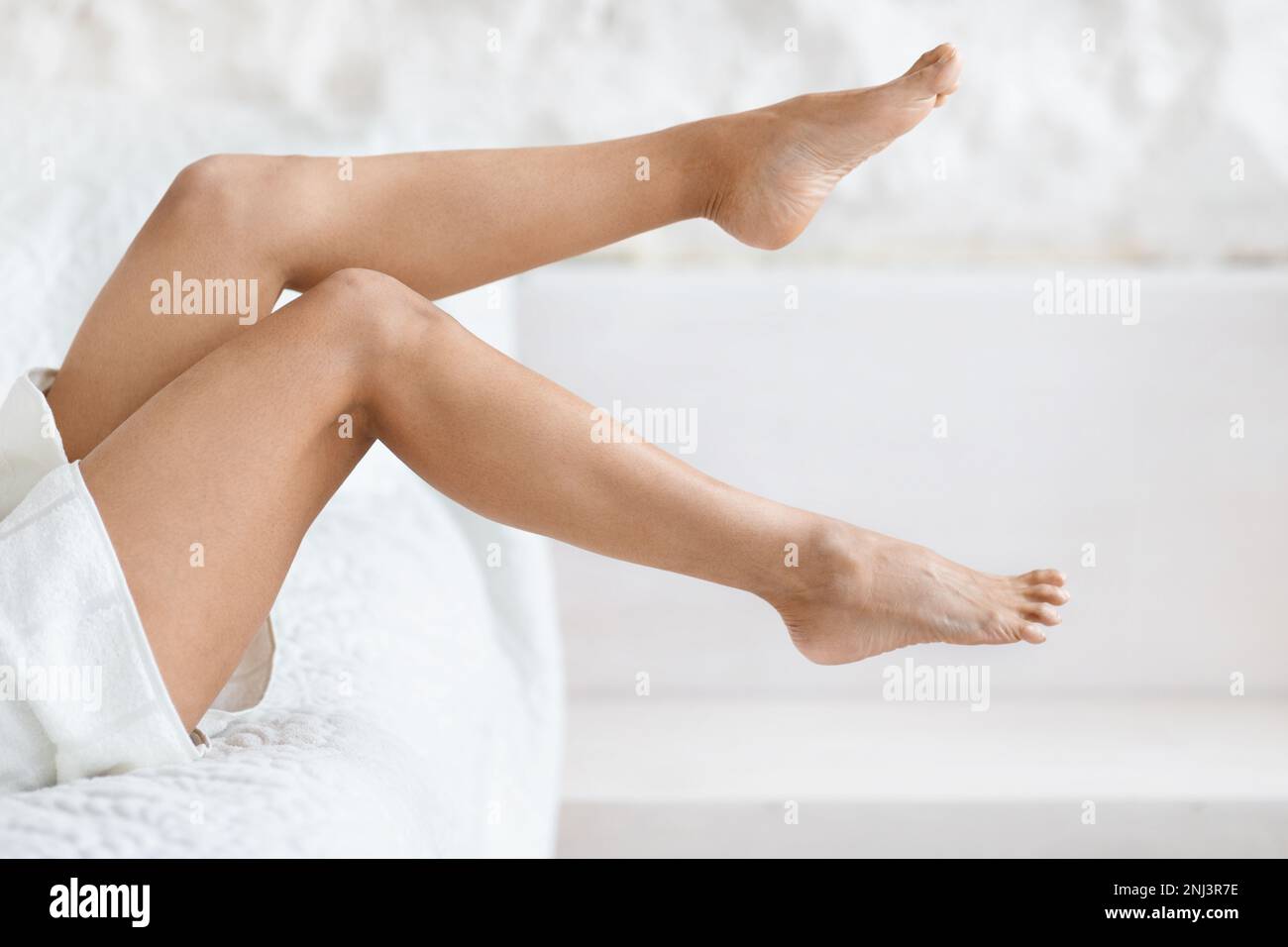 Legs of millennial caucasian lady in towel lies on bed, enjoy cleanliness, freshness at spare time Stock Photo