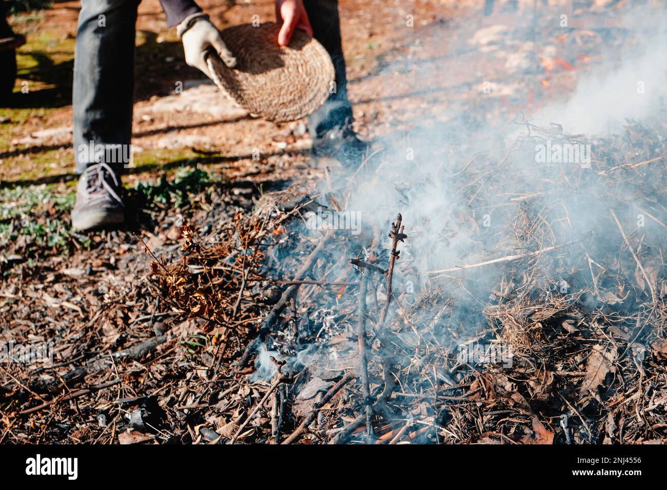 a man stokes the fire of a bonfire to burn branches, leaves and other