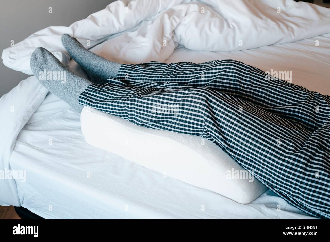 a man in bed leans his legs on a leg elevation pillow made of memory