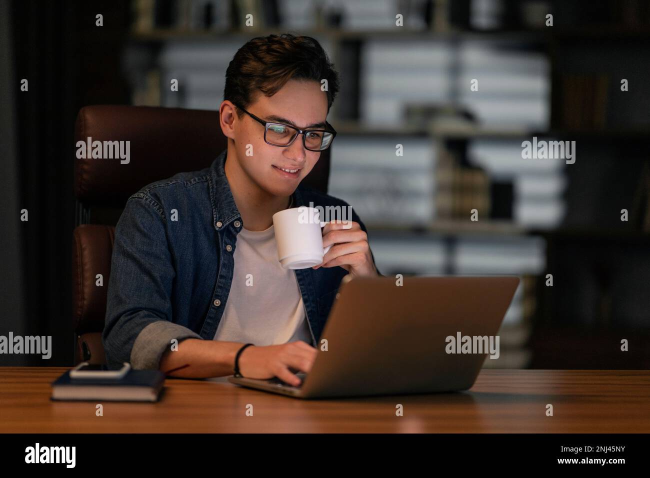 Overworked young man drinking coffee while working late at night Stock Photo