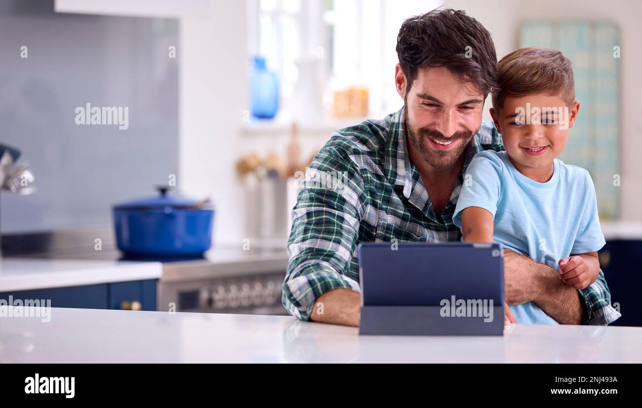 Father At Home In Kitchen With Son Using Digital Tablet Together Stock Photo