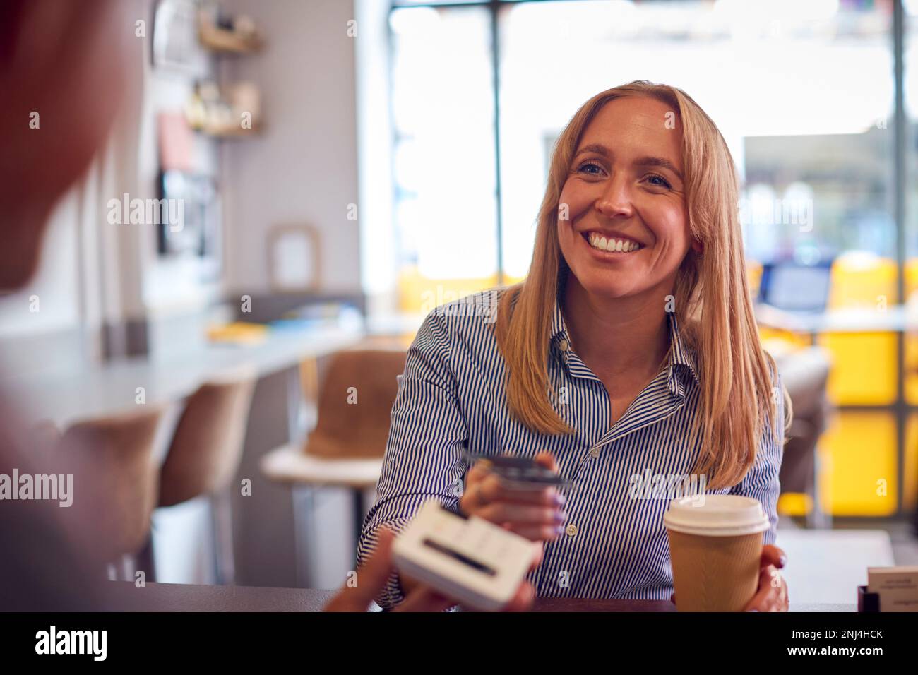 Female Customer Making Contactless Payment In Coffee Shop Using Debit Card Stock Photo