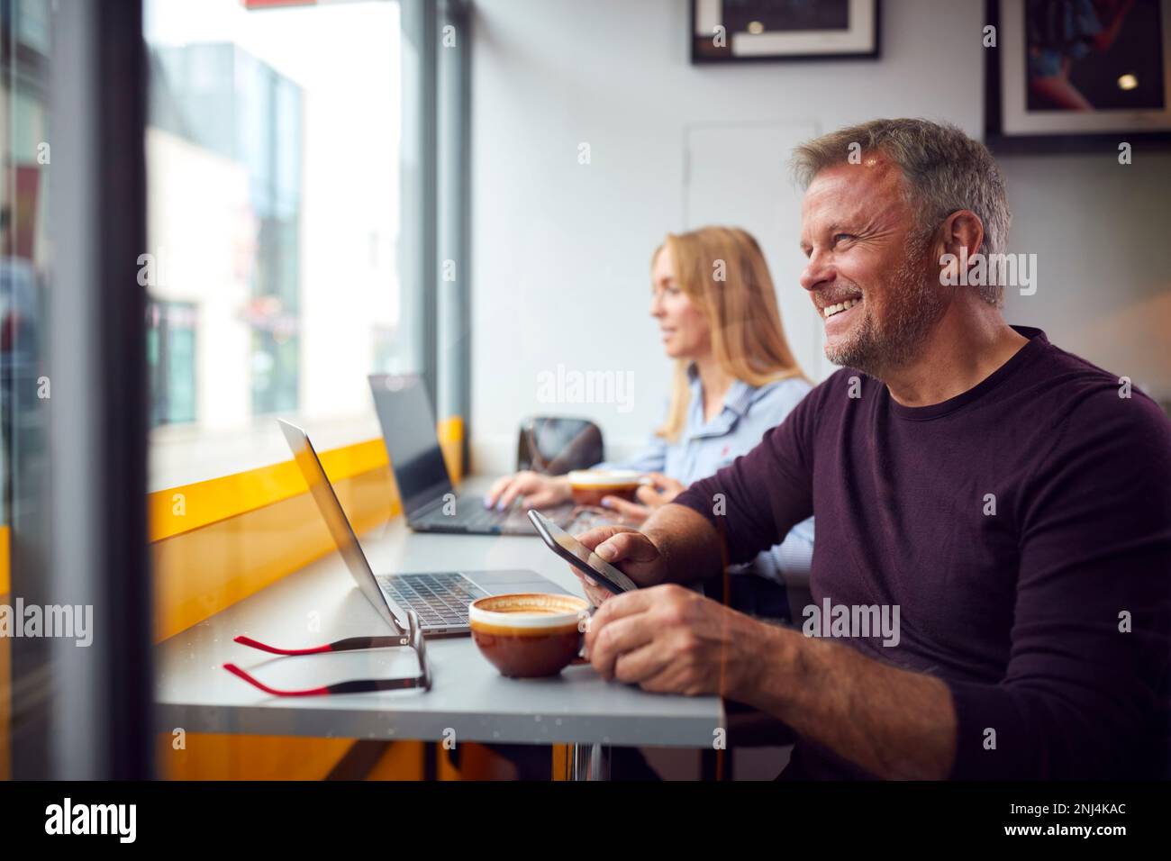 Customers In Coffee Shop Window Working On Laptops Using Mobile Phones Stock Photo