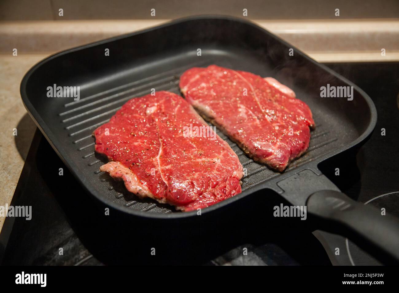 Raw minute steak of marbled beef in a grill pan on an electric cooking surface Stock Photo Alamy