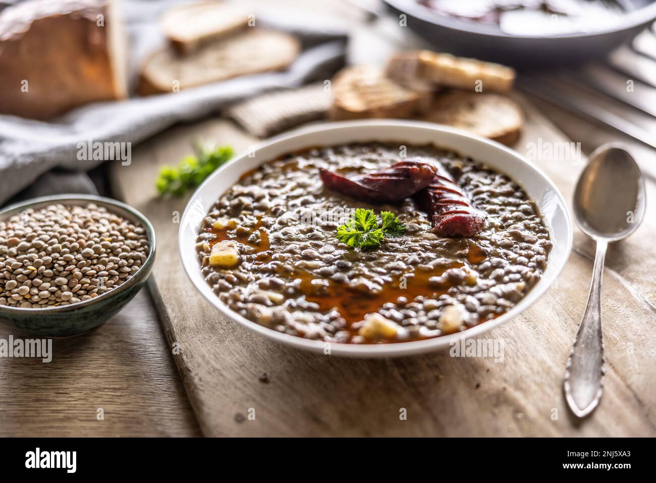 A plate full of lentil legume soup with baked sausage and fresh bread. Stock Photo