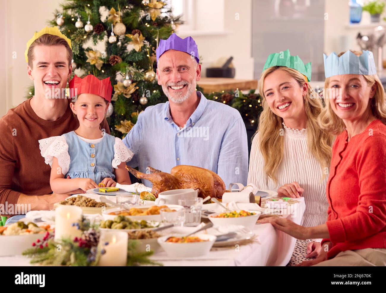 Portrait Of Multi-Generation Family Celebrating Christmas At Home Wearing Paper Hats Before Meal Stock Photo