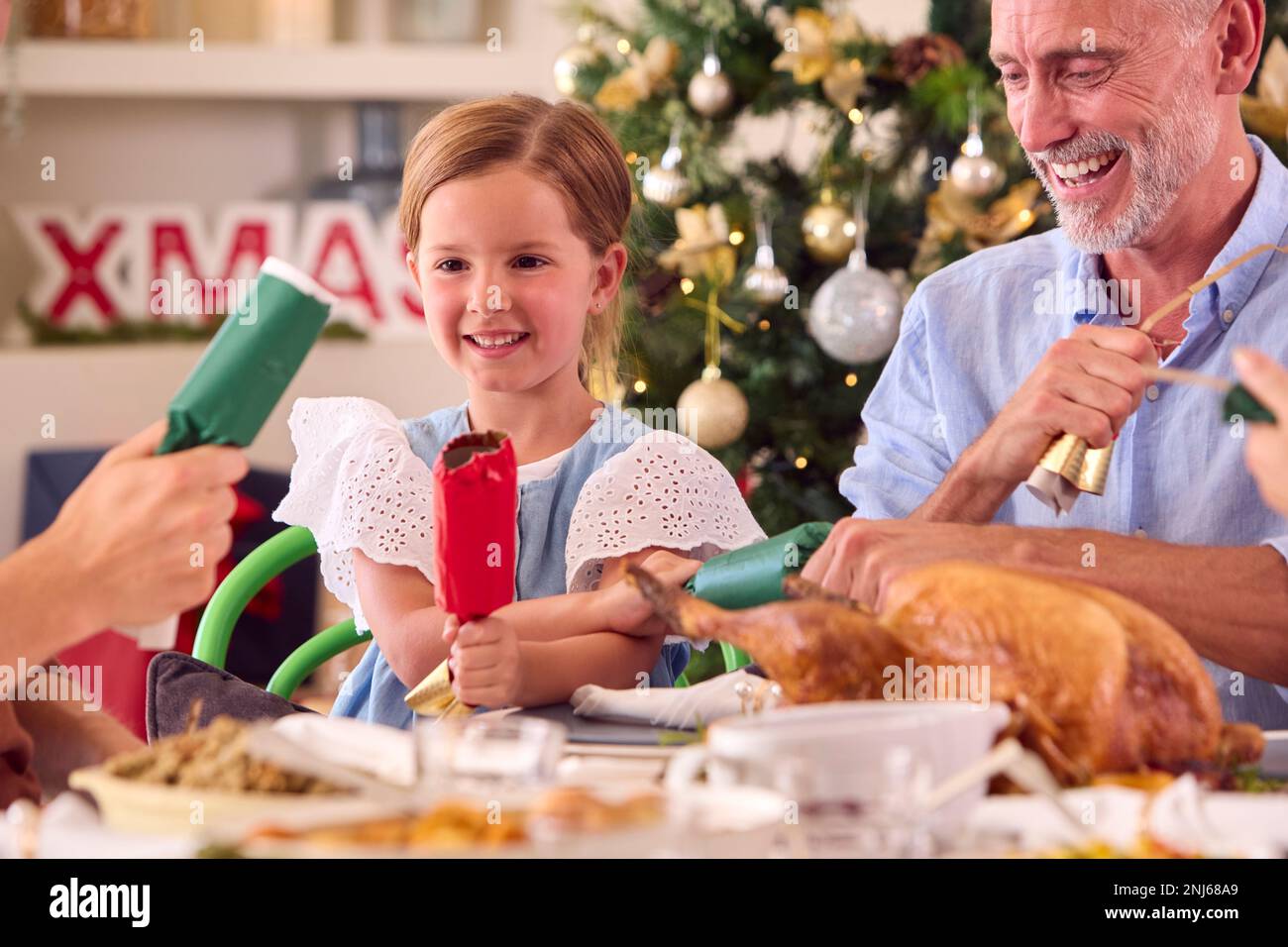 Multi-Generation Family Celebrating Christmas At Home Pulling Crackers Before Eating Meal Together Stock Photo
