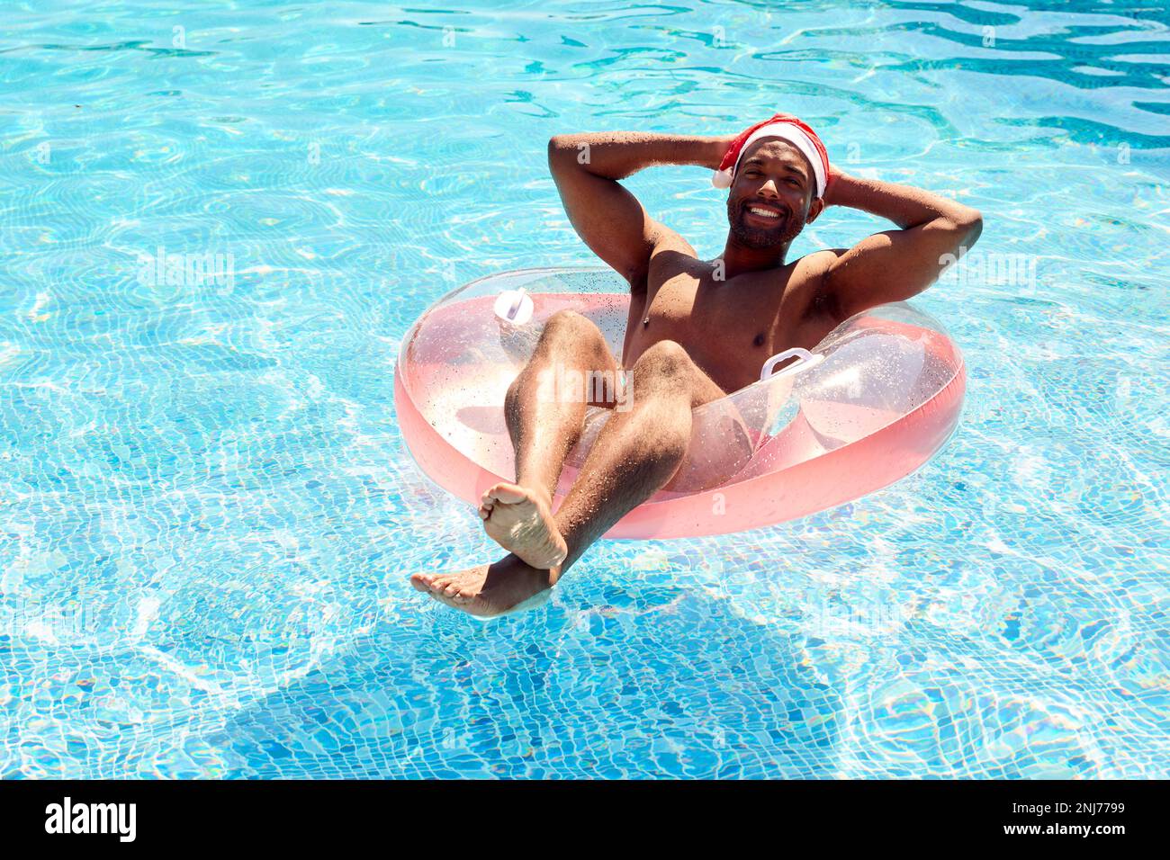 Man On Christmas Holiday Floating On Inflatable In Swimming Pool Wearing Santa Hat Stock Photo
