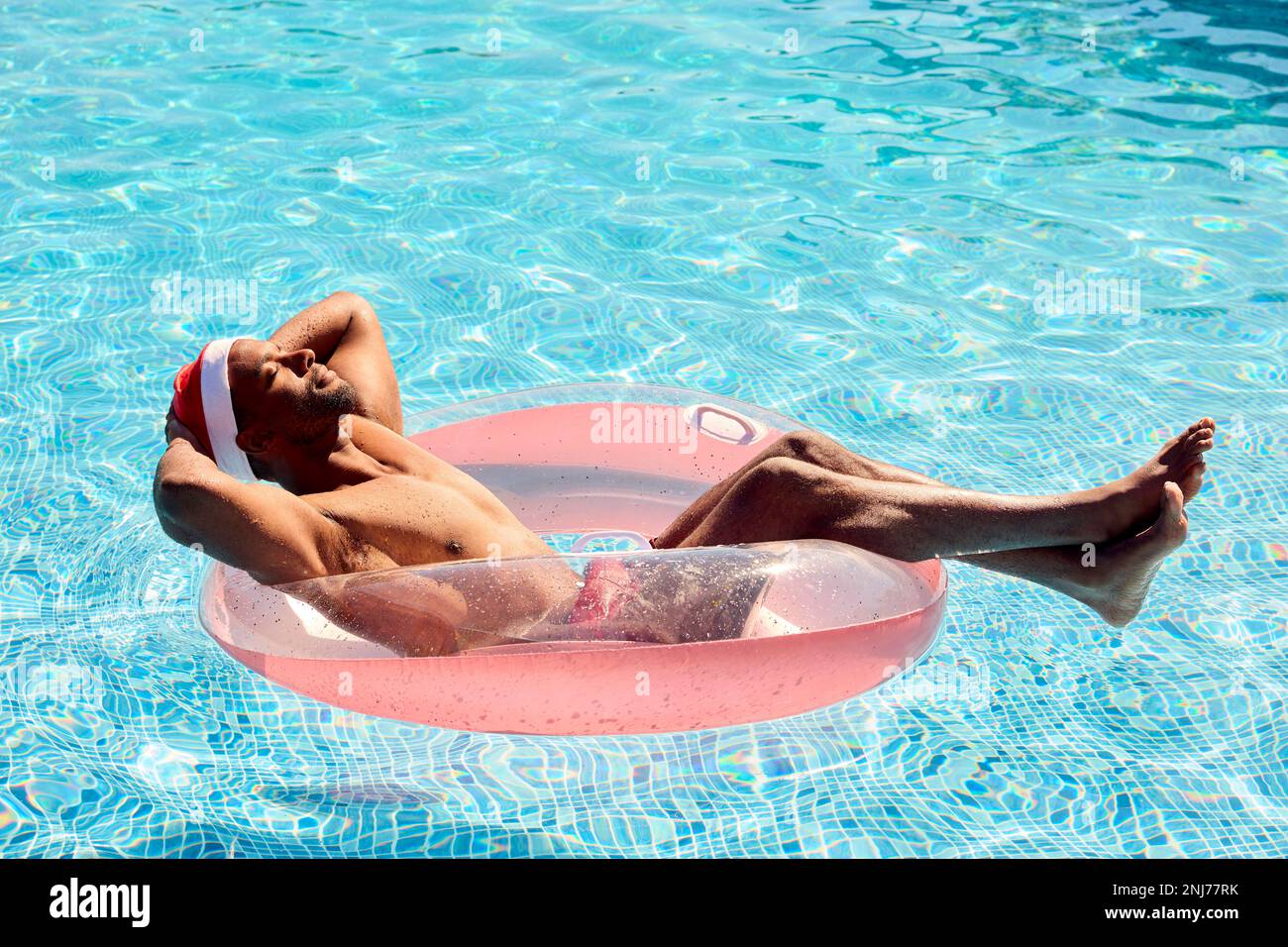 Man On Christmas Holiday Floating On Inflatable In Swimming Pool Wearing Santa Hat Stock Photo
