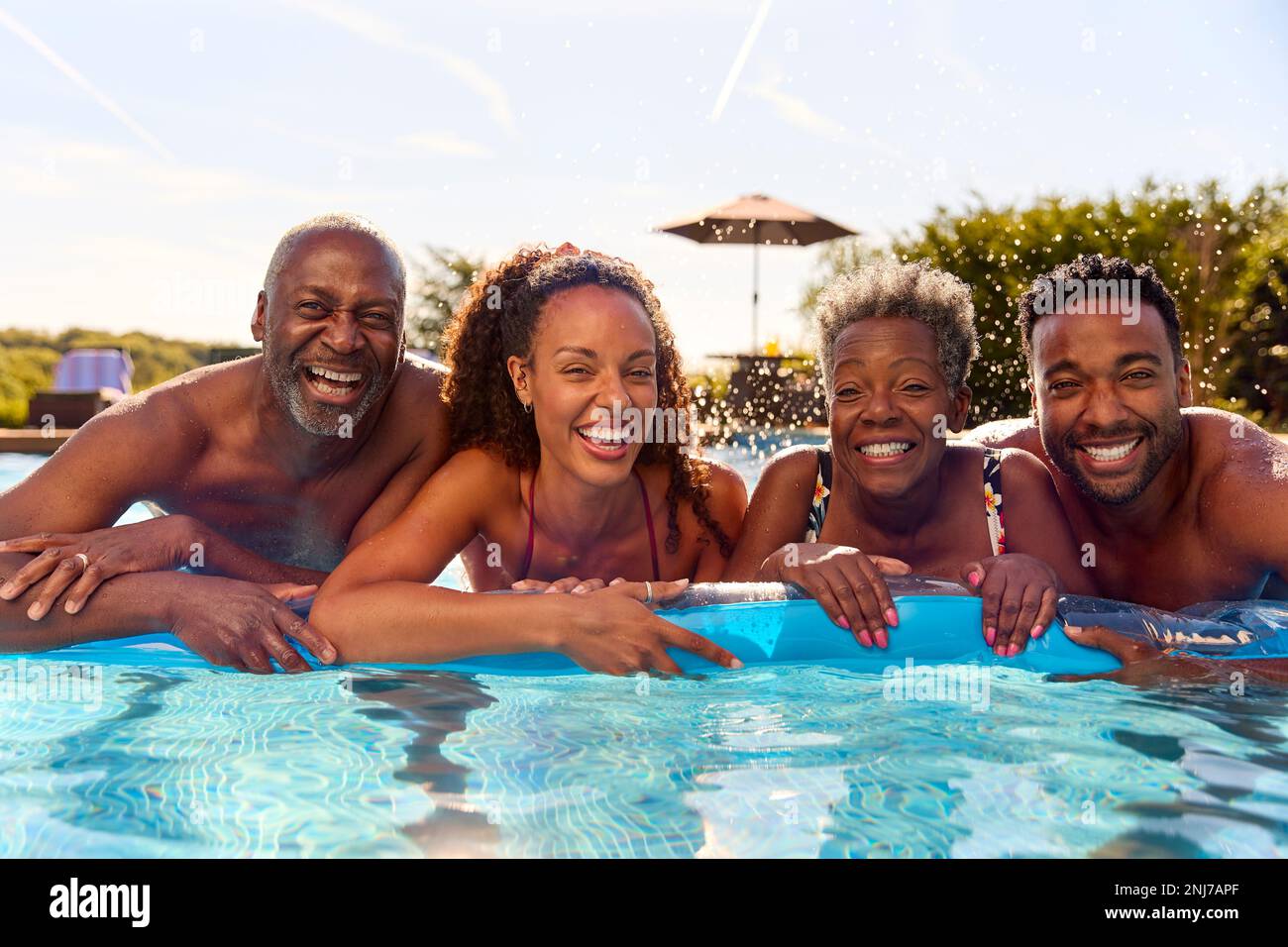 Multi-Generation Family With Adult Offspring On Summer Holiday On Inflatable In Swimming Pool Stock Photo