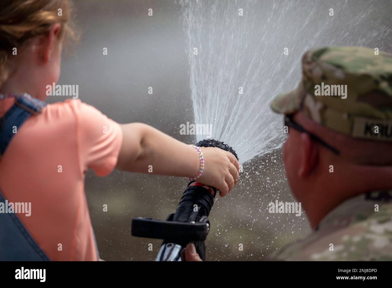 Six-year-old Birdie Amerson sprays a fire hose with the help of Sgt. Steve Krueger, 467th Engineer Battalion, Firefighter Headquarters, during an open house at Fort Des Moines, Iowa, Aug. 6, 2022. The event welcomed more than 70 people to the historic U.S Army Reserve base to see the current training units. Stock Photo