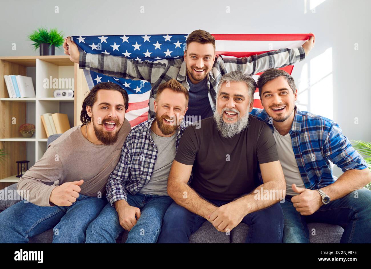 Group of men with American flag sitting on couch and watching soccer match on TV Stock Photo