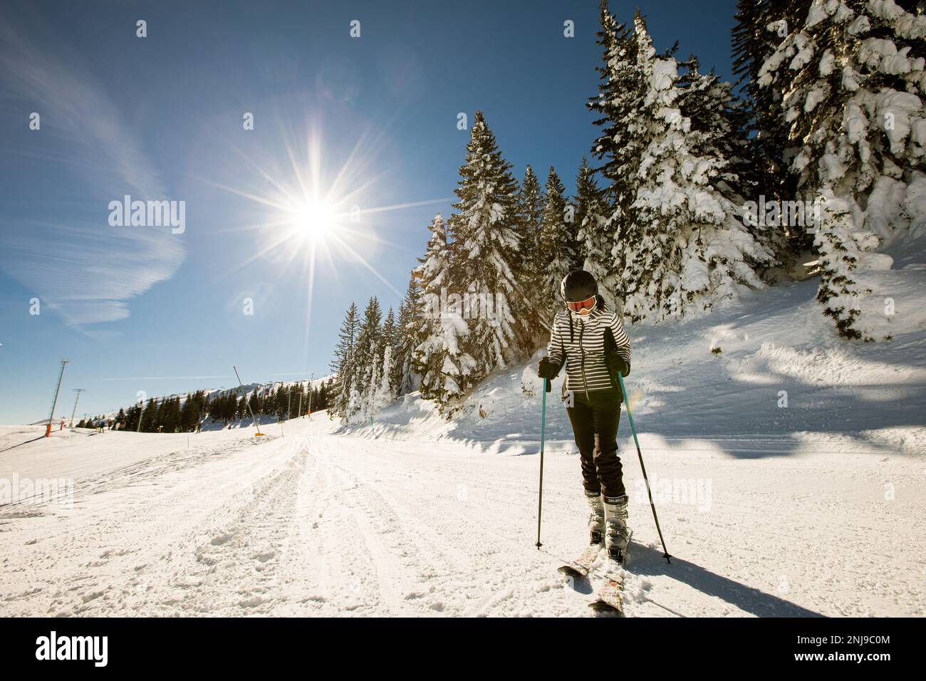 A single young female enjoys a sunny winter day of skiing, dressed in full snow gear with ski boots and sunglasses Stock Photo