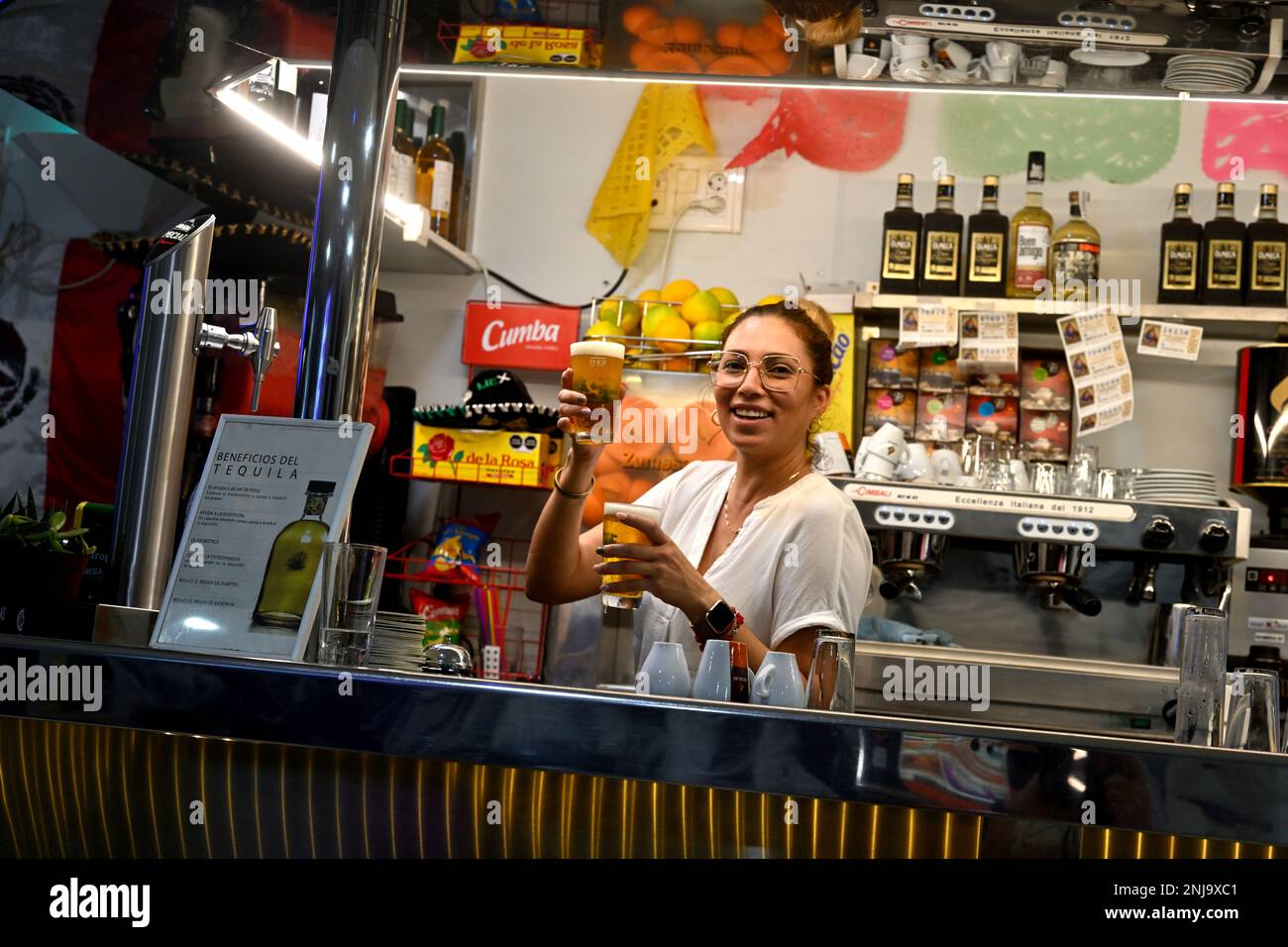 Woman bar staff behind counter holding up two glasses of beer Stock Photo