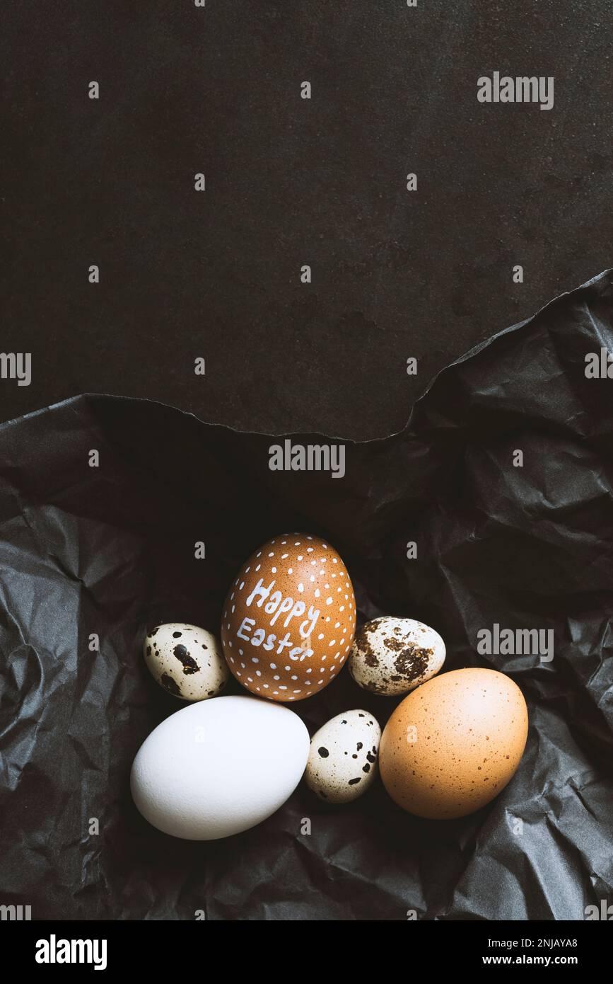 Happy easter written egg with chicken and quail eggs wrapped in black wrapping paper on black background Stock Photo