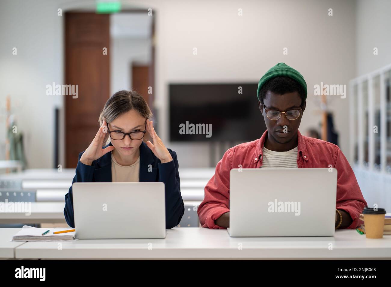 Concentrated serious students learning sitting in desktop in college lecture classroom with laptops. Stock Photo