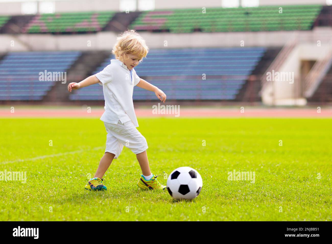Kids play football on outdoor stadium field. Children score a goal