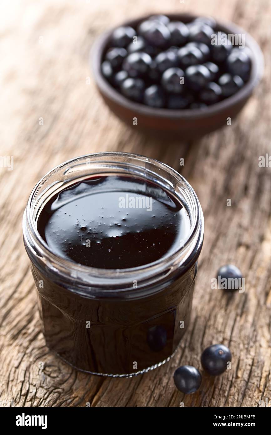 Fresh homemade jelly made of Patagonian Calafate berries (lat. Berberis heterophylla) in glass jar,  raw berries on the side and in the back Stock Photo