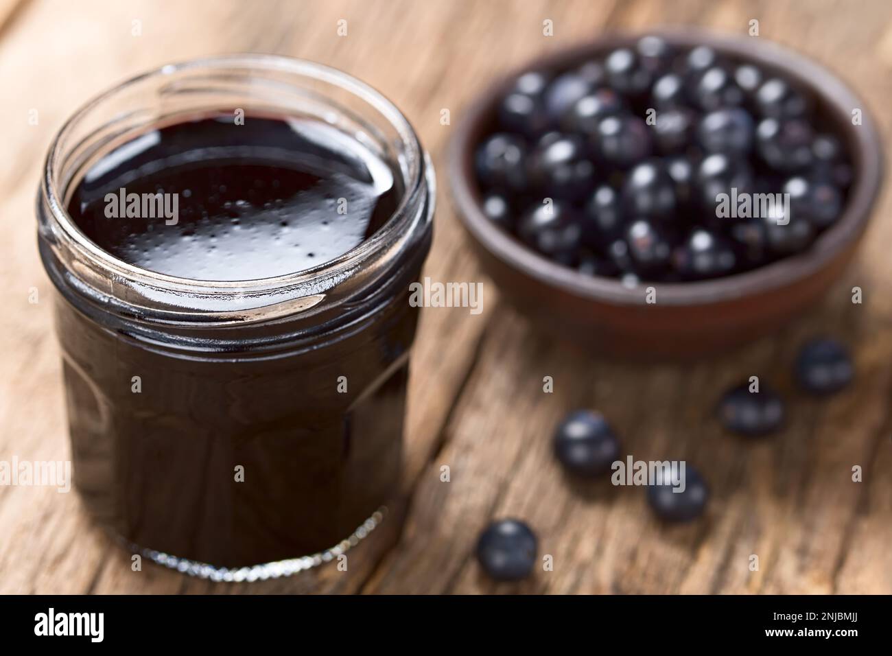 Fresh homemade jelly made of Patagonian Calafate berries (lat. Berberis heterophylla) in glass jar,  raw berries on the side and in the back Stock Photo