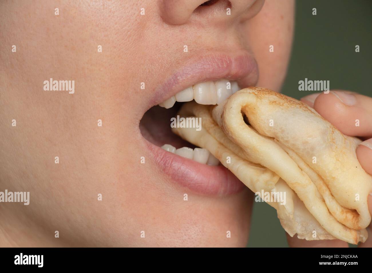 girl's mouth bites a pancake closeup Stock Photo