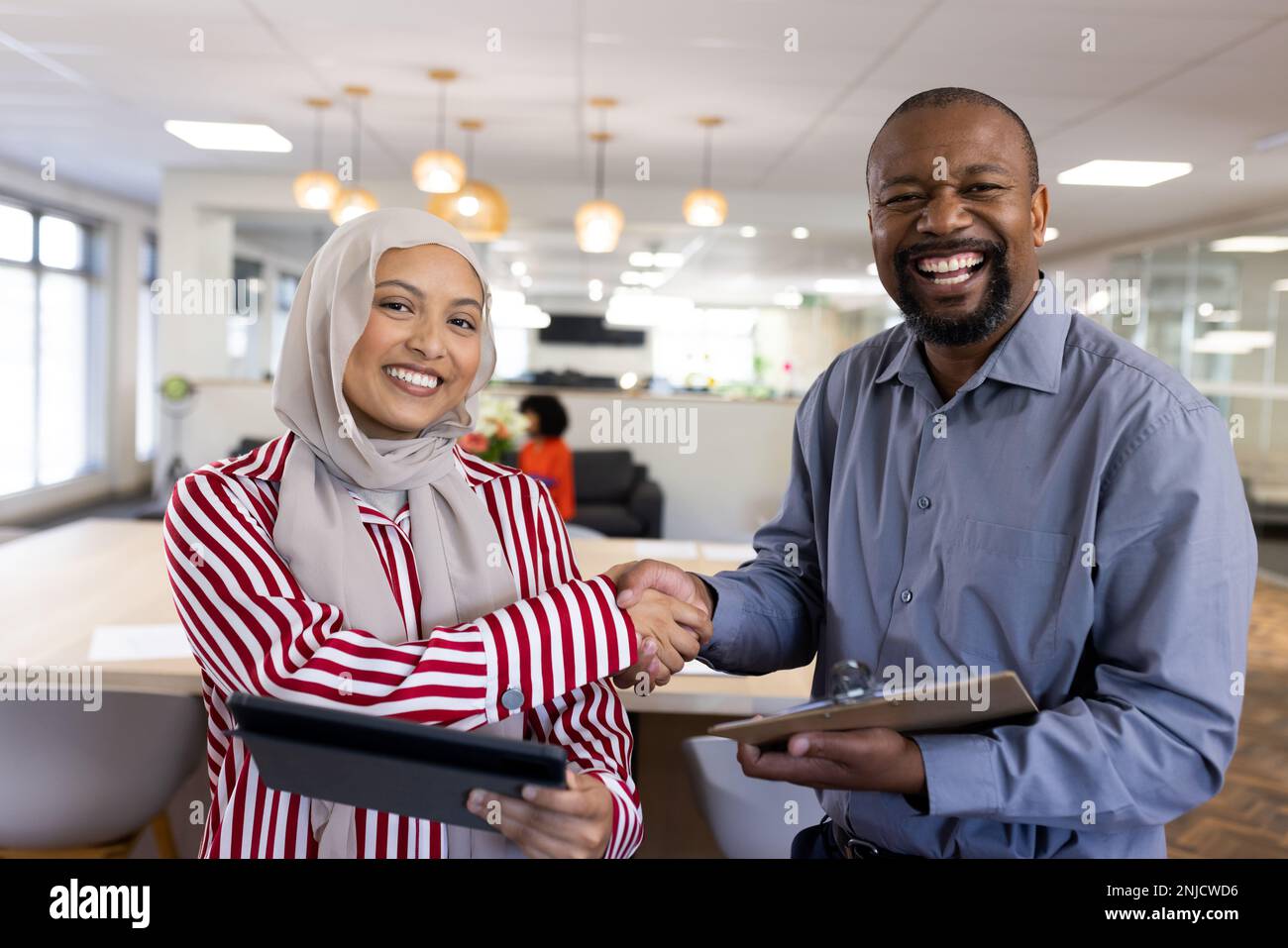 Happy diverse female and male business people shaking hands and looking at camera in office Stock Photo