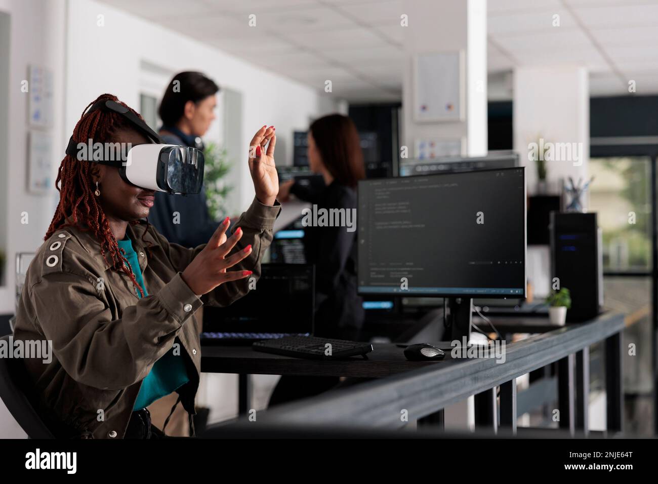 African american system engineer wearing virtual reality goggles working to develop security program in it big data office, software developer with vr headset coding html script with database. Stock Photo