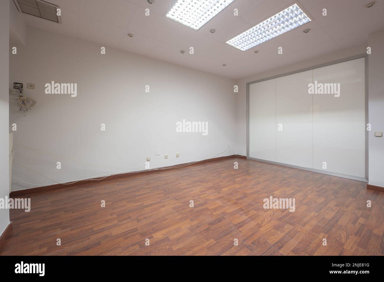 An empty office with technical ceilings, a glass partition and reddish floating floorboards Stock Photo