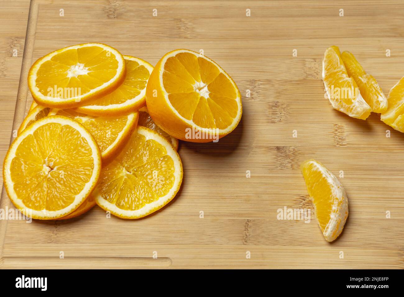 Sliced ripe oranges, orange segments and an orange split in half on a bamboo wooden surface Stock Photo