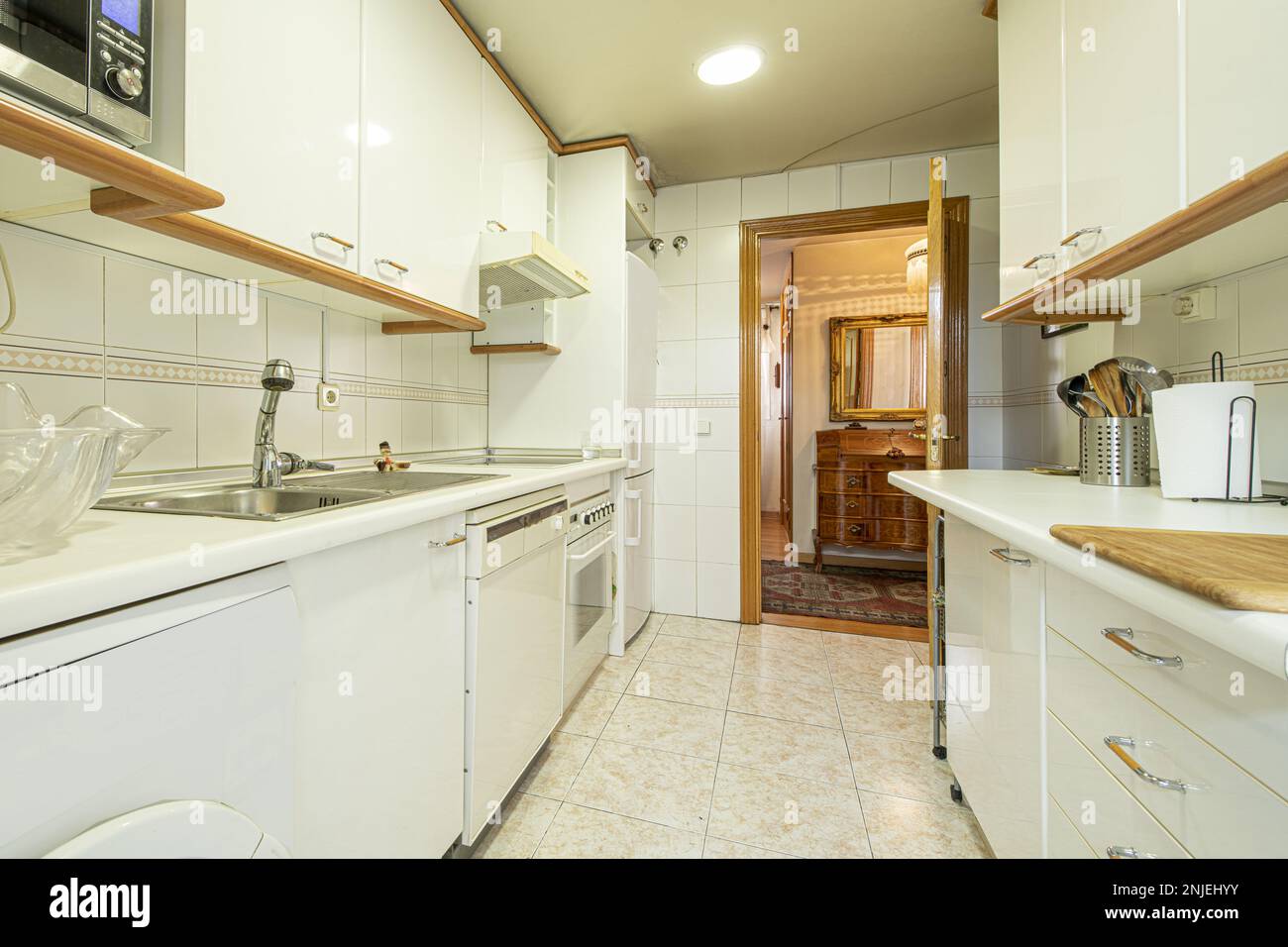 Kitchen with white furniture with metal and wood handles to match cornices and moldings, electromesivos of various integrated whites and light tiles Stock Photo