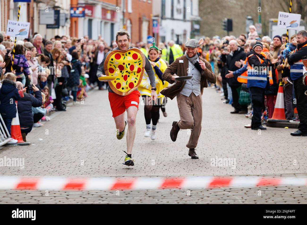 The annual Shrove Tuesday pancake race held in Lichfield, Staffordshire, England. The event comprises of childrens races, a mascot race and male and female races. The event starts at noon and is compered by the town crier and judged by he Lord Mayor. Pictured left, wearing pancake, winner of the mascot fun event Austin Brauser from the WIP running club. Stock Photo