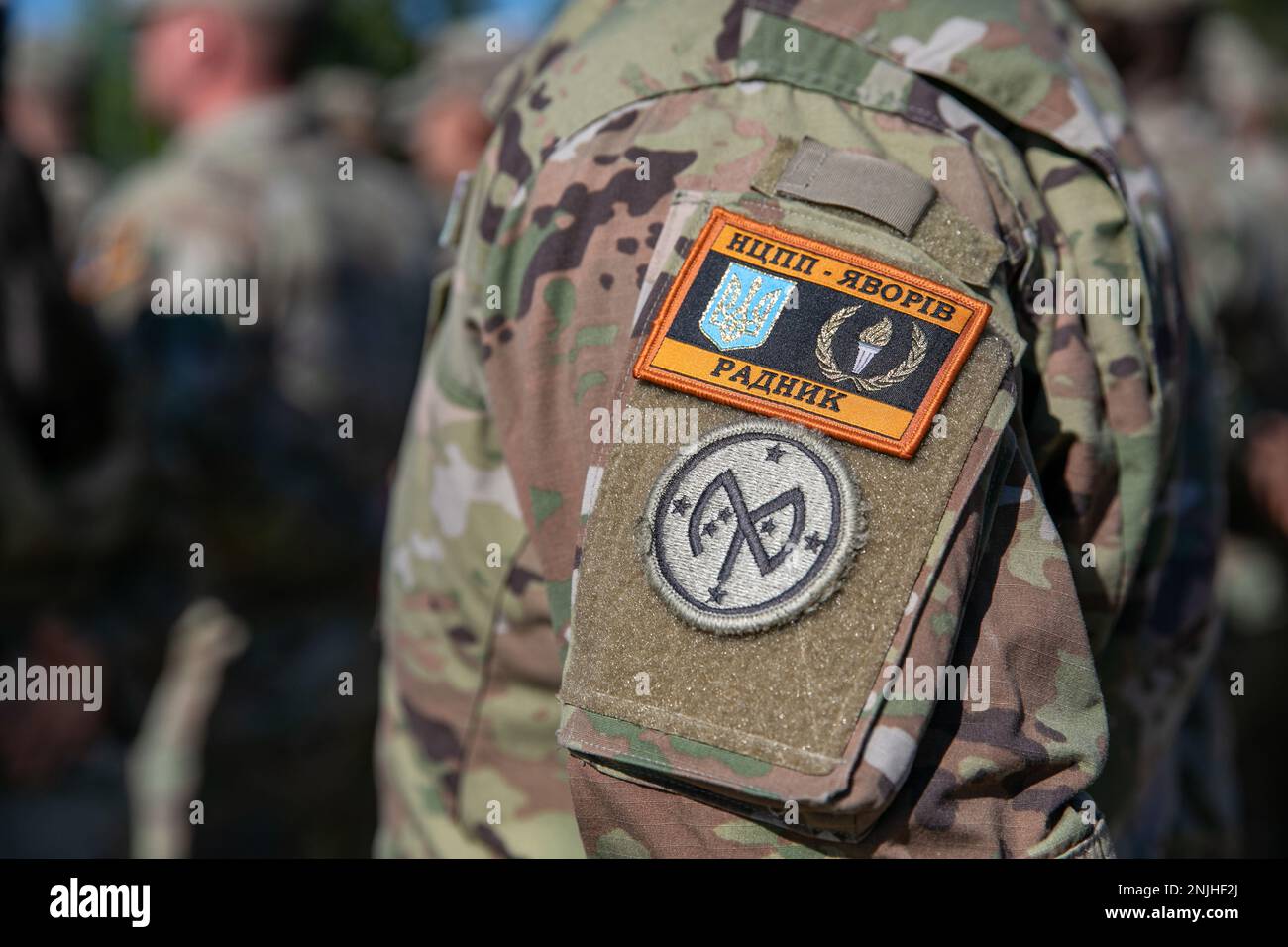 A U.S. Army Soldier assigned to Task Force Orion, 27th Infantry Brigade Combat Team, New York Army National Guard, wears the Combat Training Center-Yavoriv Advisor patch above the 27th IBCT patch during the Joint Multinational Training Group-Ukraine Transfer of Authority ceremony in Grafenwoehr, Germany, August 8, 2022. Task Force Orion assumed the JMTG-U mission from Task Force Gator, 53rd IBCT, Florida Army National Guard, and will continue to ensure the combat effectiveness of Ukrainian military personnel training on systems and equipment issued under the United States’ Presidential Drawdow Stock Photo