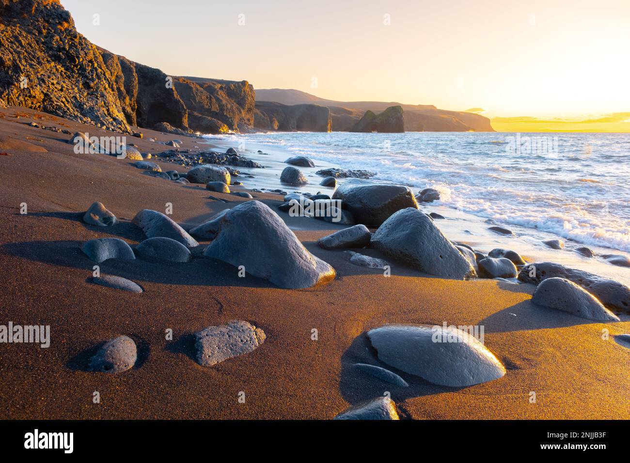 Scenic beach with black sand by low tide at sunset, Sharp mountain volcanic cliffs on Atlantic ocean coastline, Famous touristic place in Iceland Stock Photo