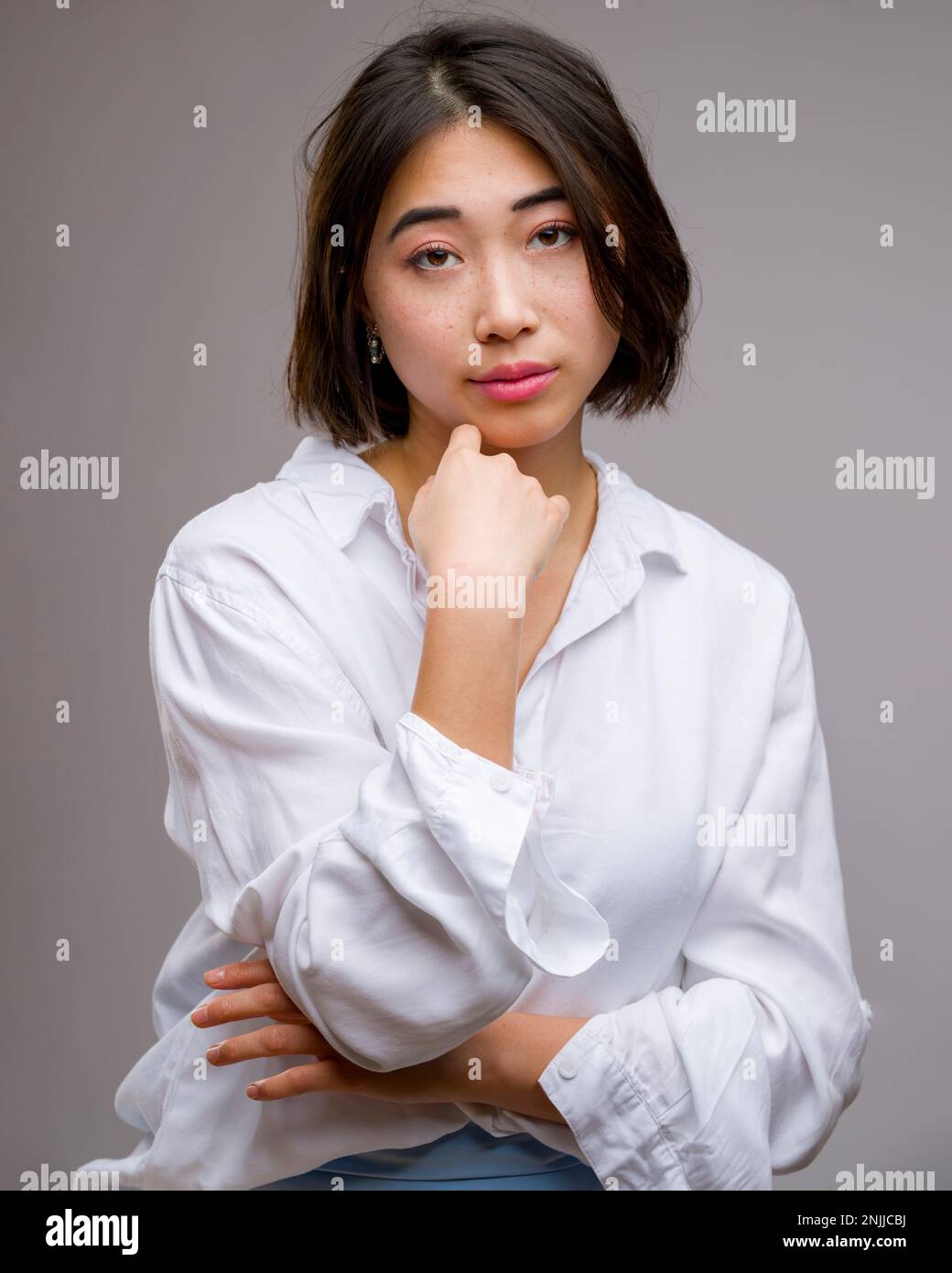 Half Body Portrait of Young Beautiful Asian Woman Standing in Front of White Background | Arms wrapped around chest Stock Photo