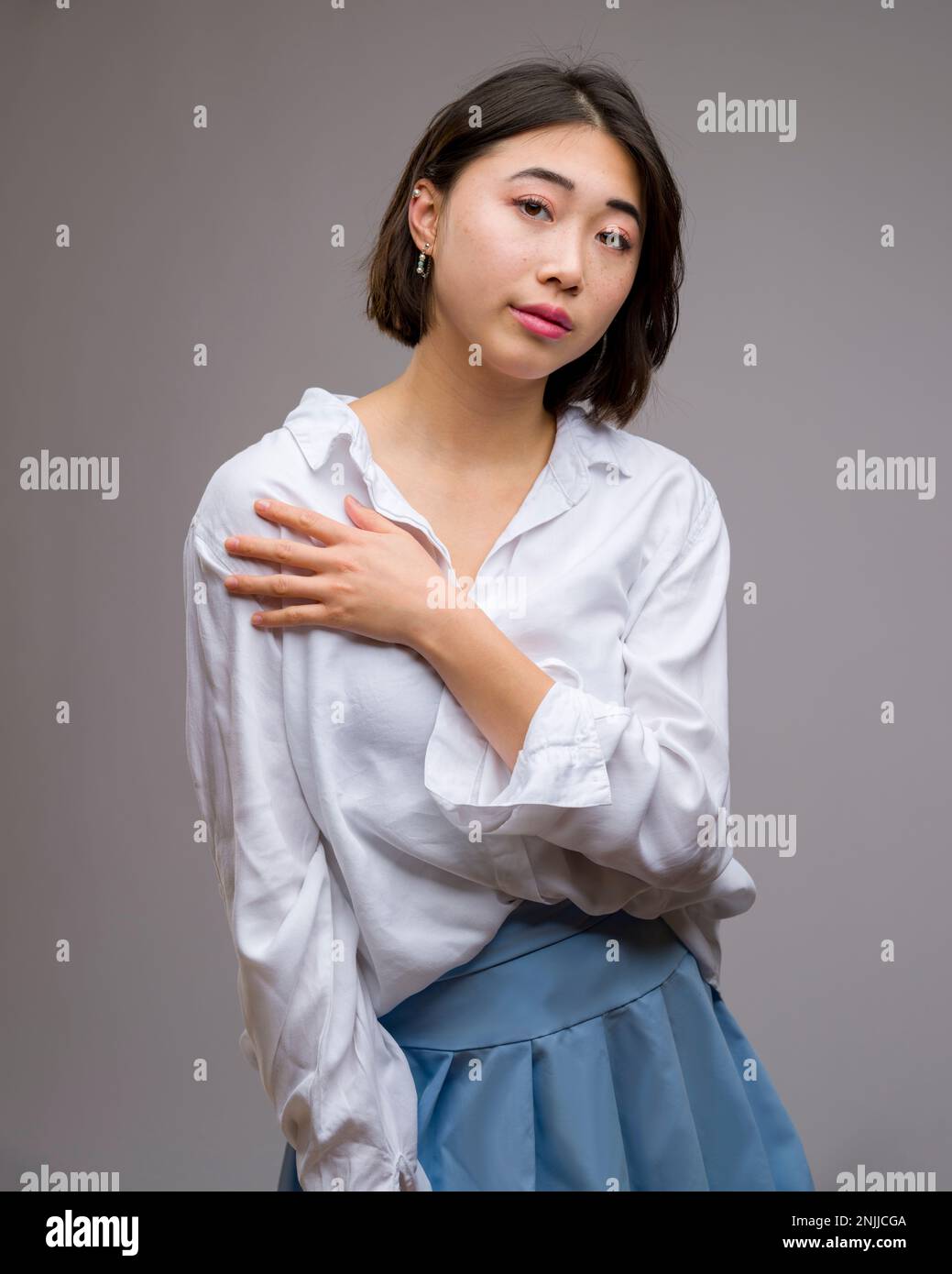 Half Body Portrait of Young Beautiful Asian Woman Standing in Front of White Background | Arms wrapped around chest Stock Photo