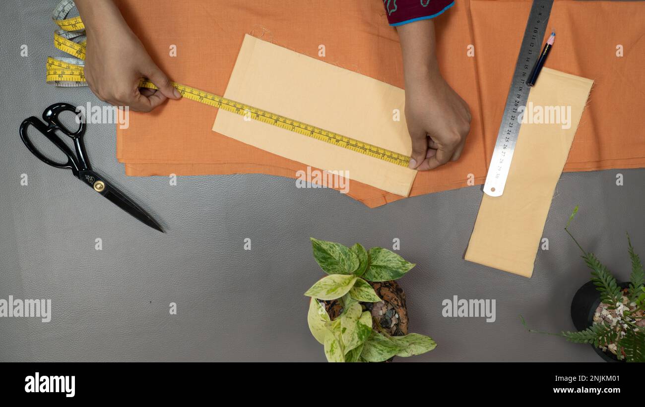 Hand measuring fabric with tape on a gray background. sewing project top view Stock Photo