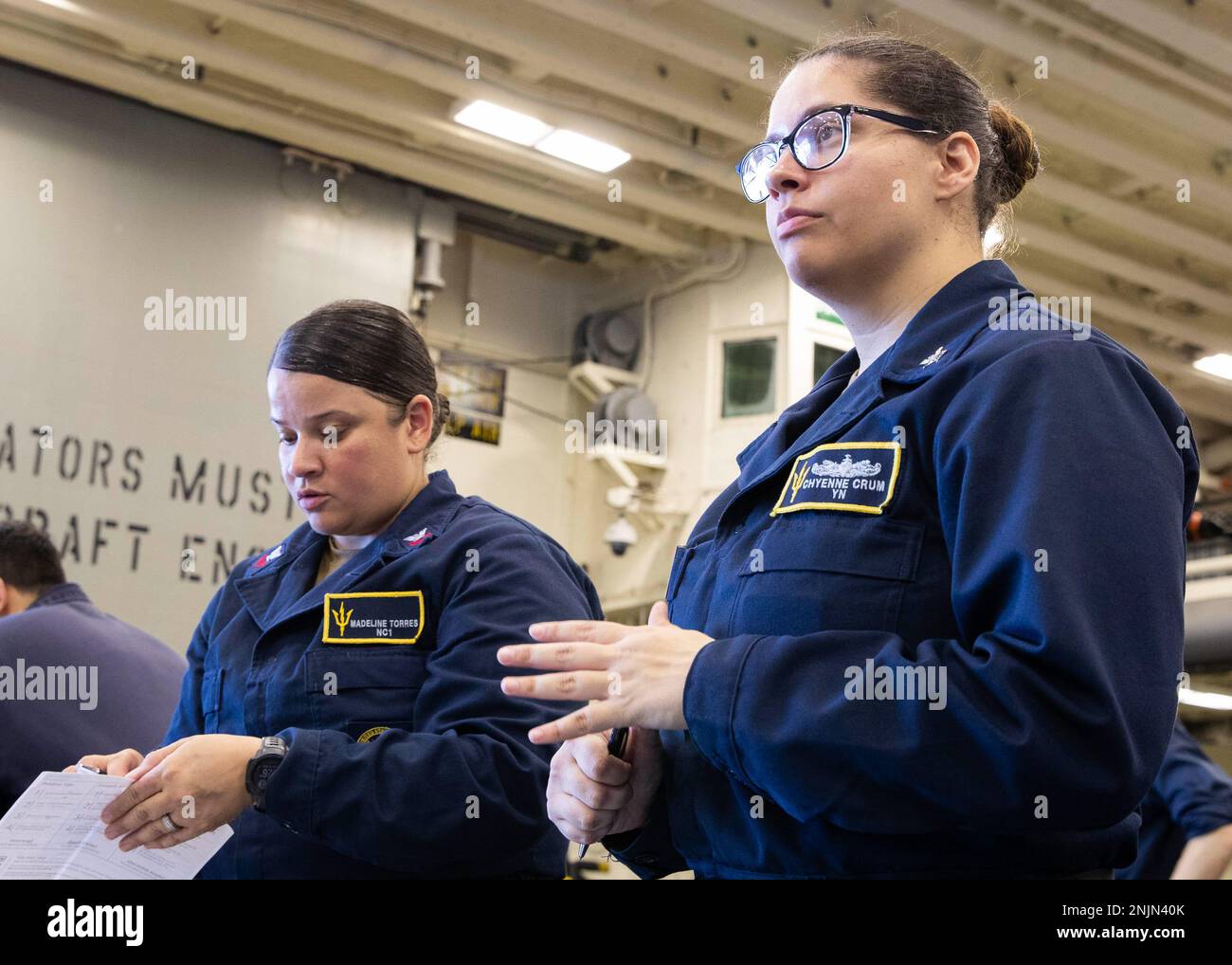 220810-N-TT639-1174 PHILIPPINE SEA (Aug. 10, 2022) – Navy Counselor 1st Class Madeline Torres, from Perth Amboy, New Jersey, left, and Yeoman 2nd Class Chyenne Crum, from Tallahassee, Florida, issue badges during non-combatant evacuation operation drill in the hangar bay aboard amphibious assault carrier USS Tripoli (LHA 7), Aug. 10, 2022. Tripoli is operating in the U.S. 7th Fleet area of operations to enhance interoperability with allies and partners and serve as a ready response force to defend peace and maintain stability in the Indo-Pacific region. Stock Photo