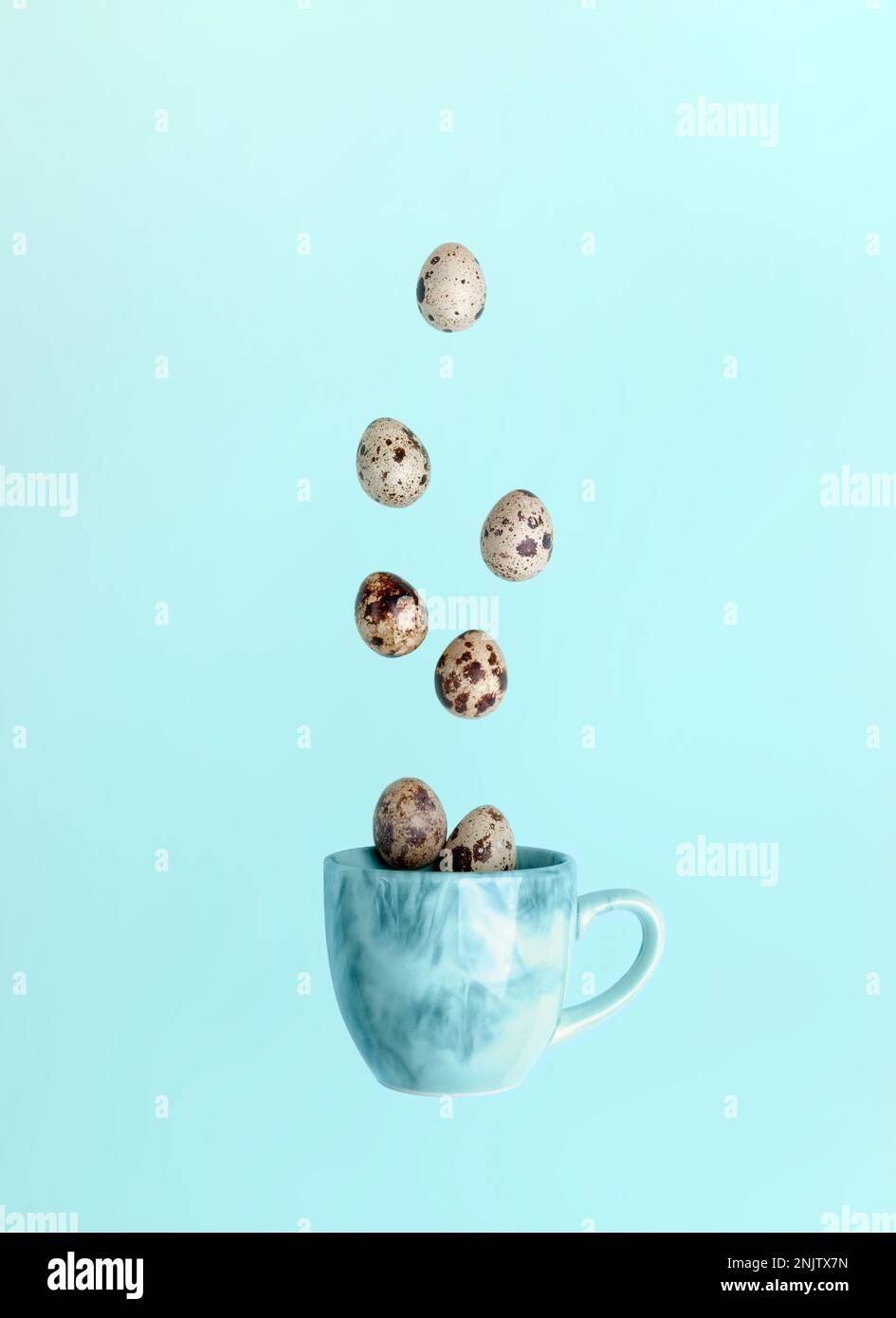 Easter minimal creative card. Quail eggs and falling to blue cup on light blue background. Falling food image. Creative advertising of healthy food. T Stock Photo