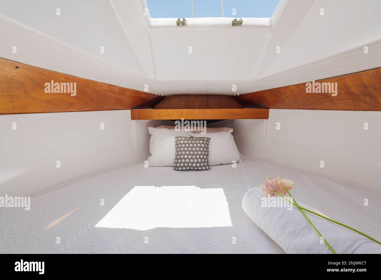 Bright luxury comfortable yacht inside with wood trim with white terry sheets, pillows, flower and sunbeams breaking through. Concept of luxury Stock Photo