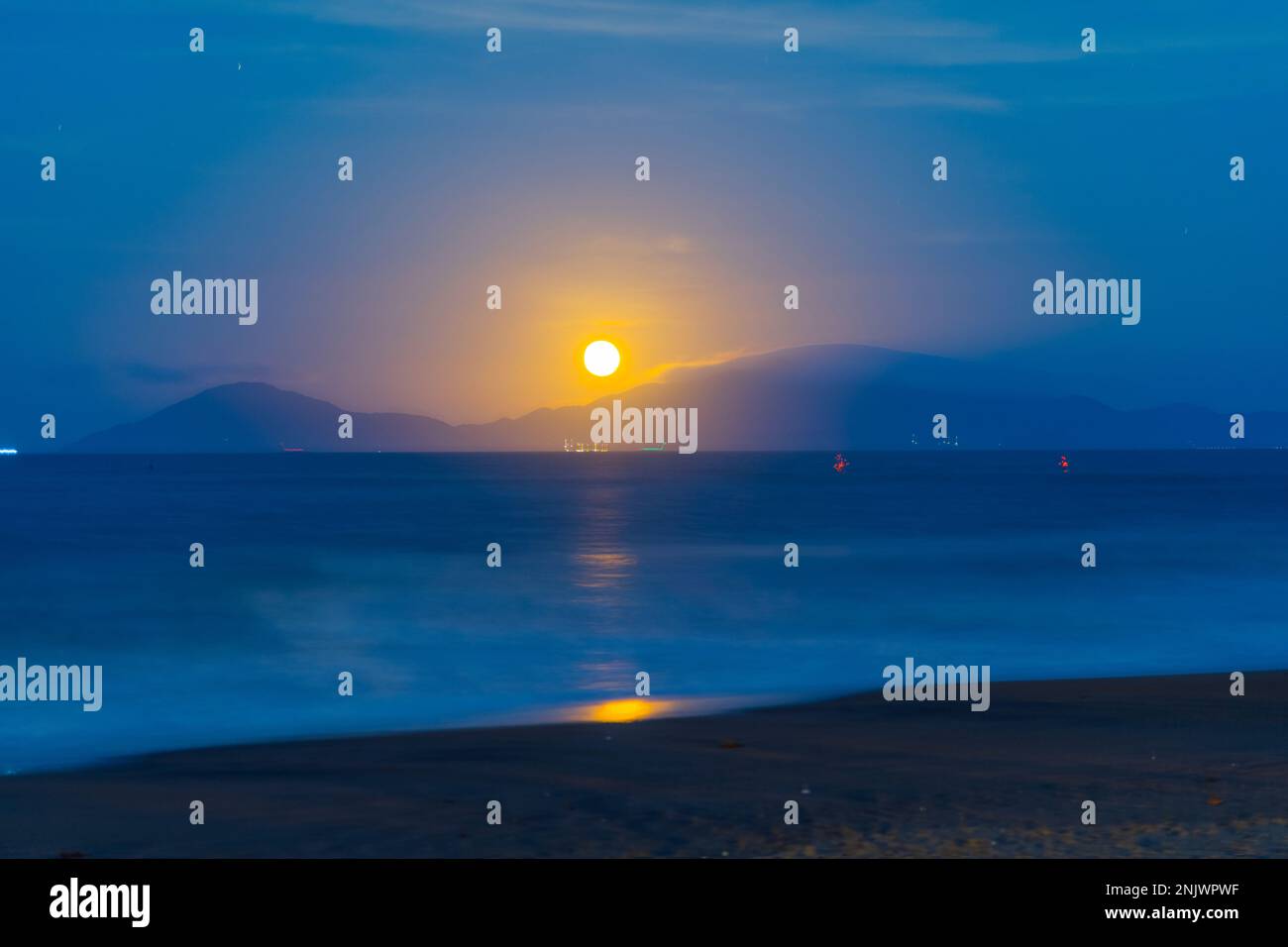 Blue hour as the moon rises full moon rises over cham island across the ocean. Stock Photo