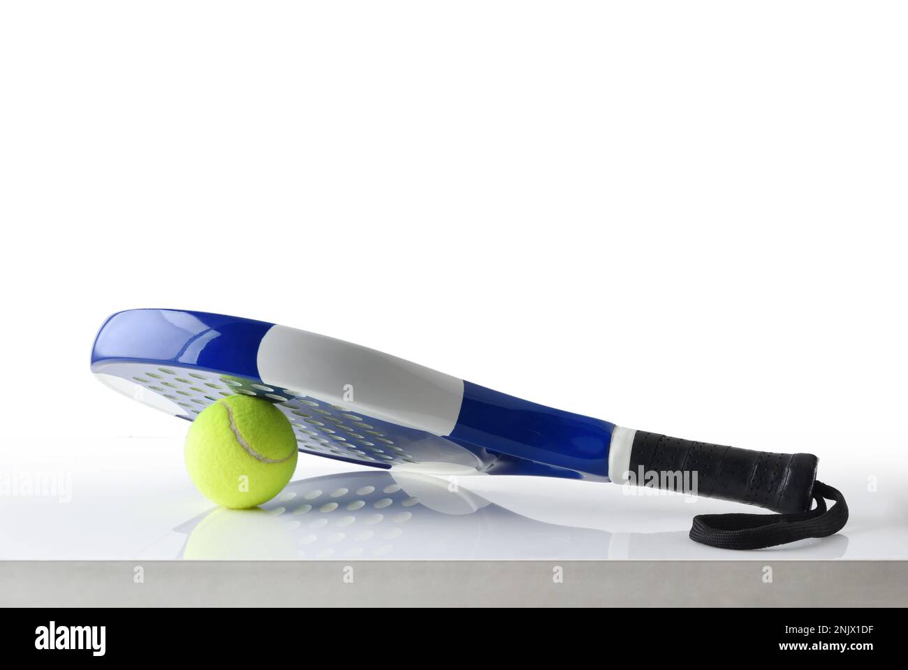 Padel racket on ball reflected on white table and white isolated background. Front view. Stock Photo