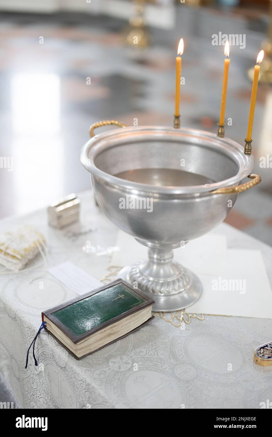 Baptismal font with blessing water and wax candles is on the table