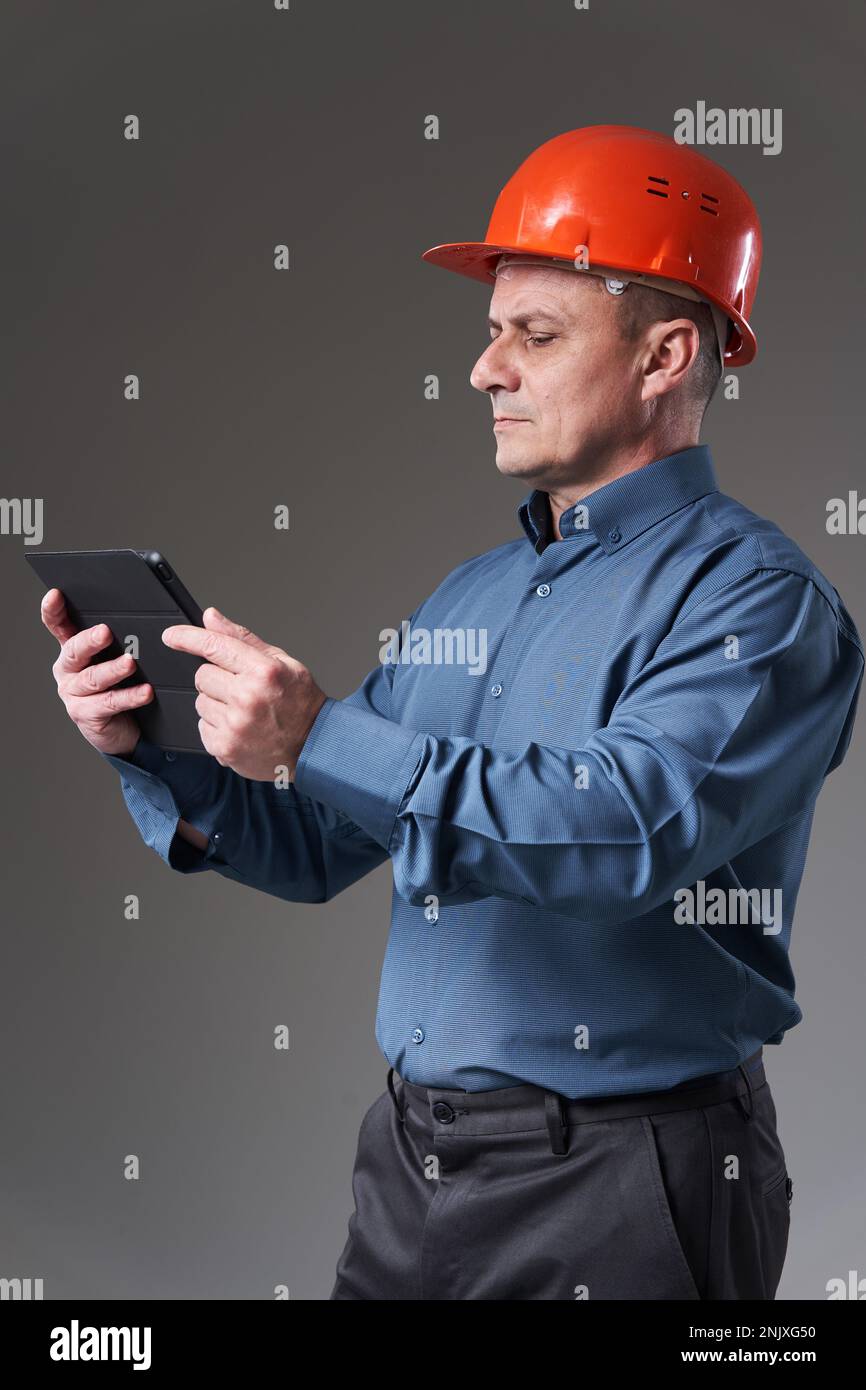 Engineer in hardhat doing planning digitally with a tablet, isolated on gray background Stock Photo