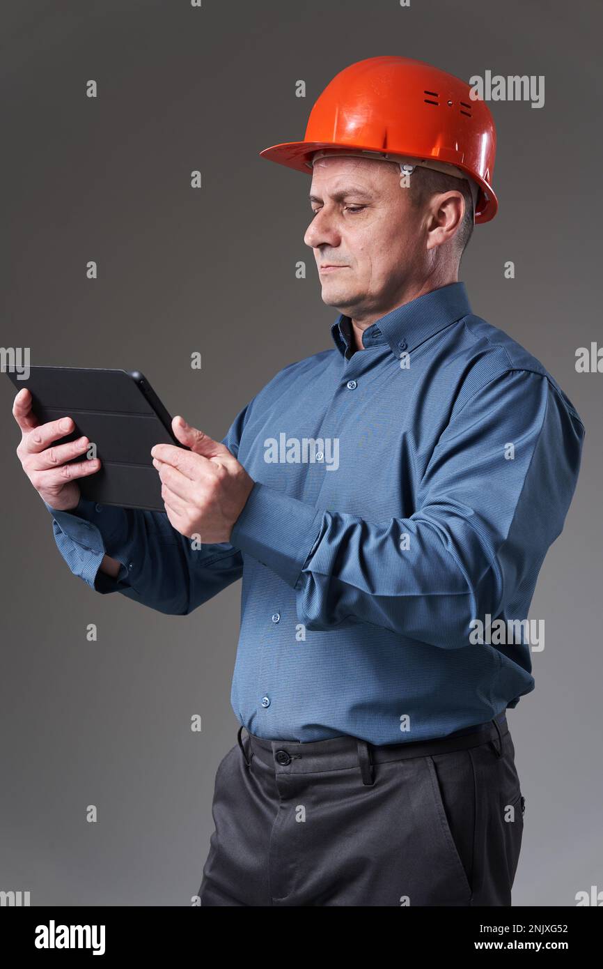 Engineer in hardhat doing planning digitally with a tablet, isolated on gray background Stock Photo
