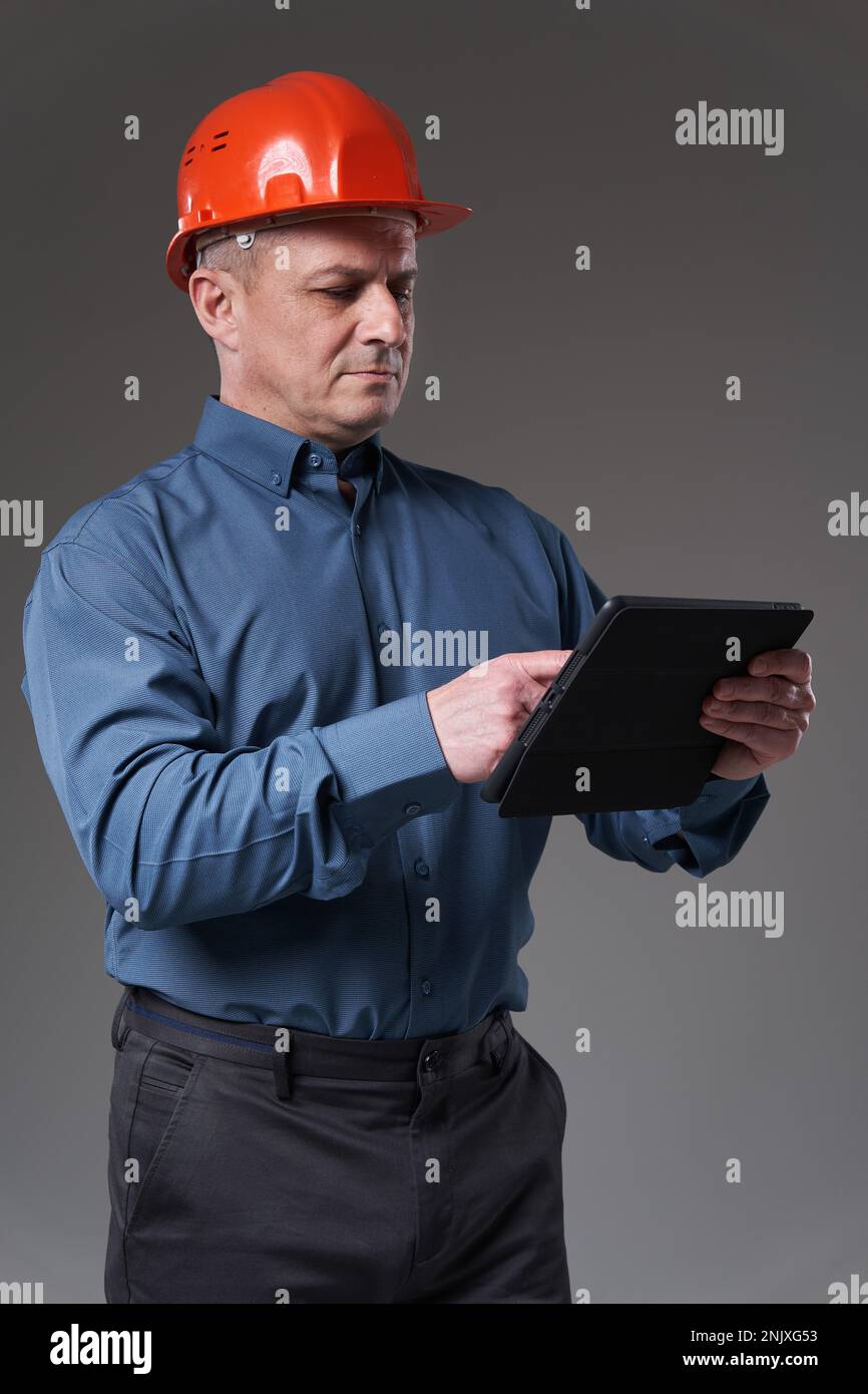 Engineer in hardhat doing planning digitally with a tablet, isolated on gray background Stock Photo